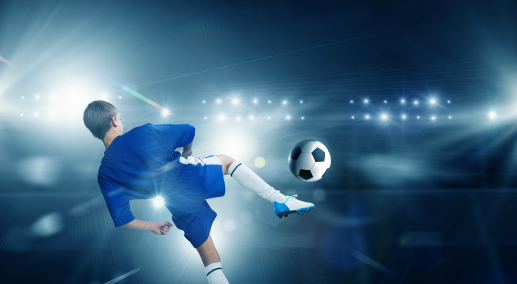 Rear view of kid boy in blue uniform on soccer stadium kicking ball